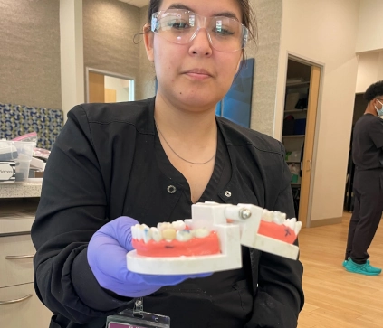 Pearland DAS student holding up a finished temporary crown model with gloves during lab practice